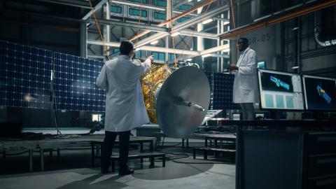 Deux personnes en blouse blanche travaillant sur un satellite 